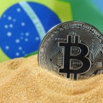 Moeda de bitcoin na areia com a bandeira do Brasil no fundo
