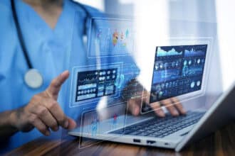 Profissional de saúde utilizando um laptop com interfaces gráficas de dados médicos e segurança cibernética holográficas, destacando a importância da cibersegurança no setor da saúde.