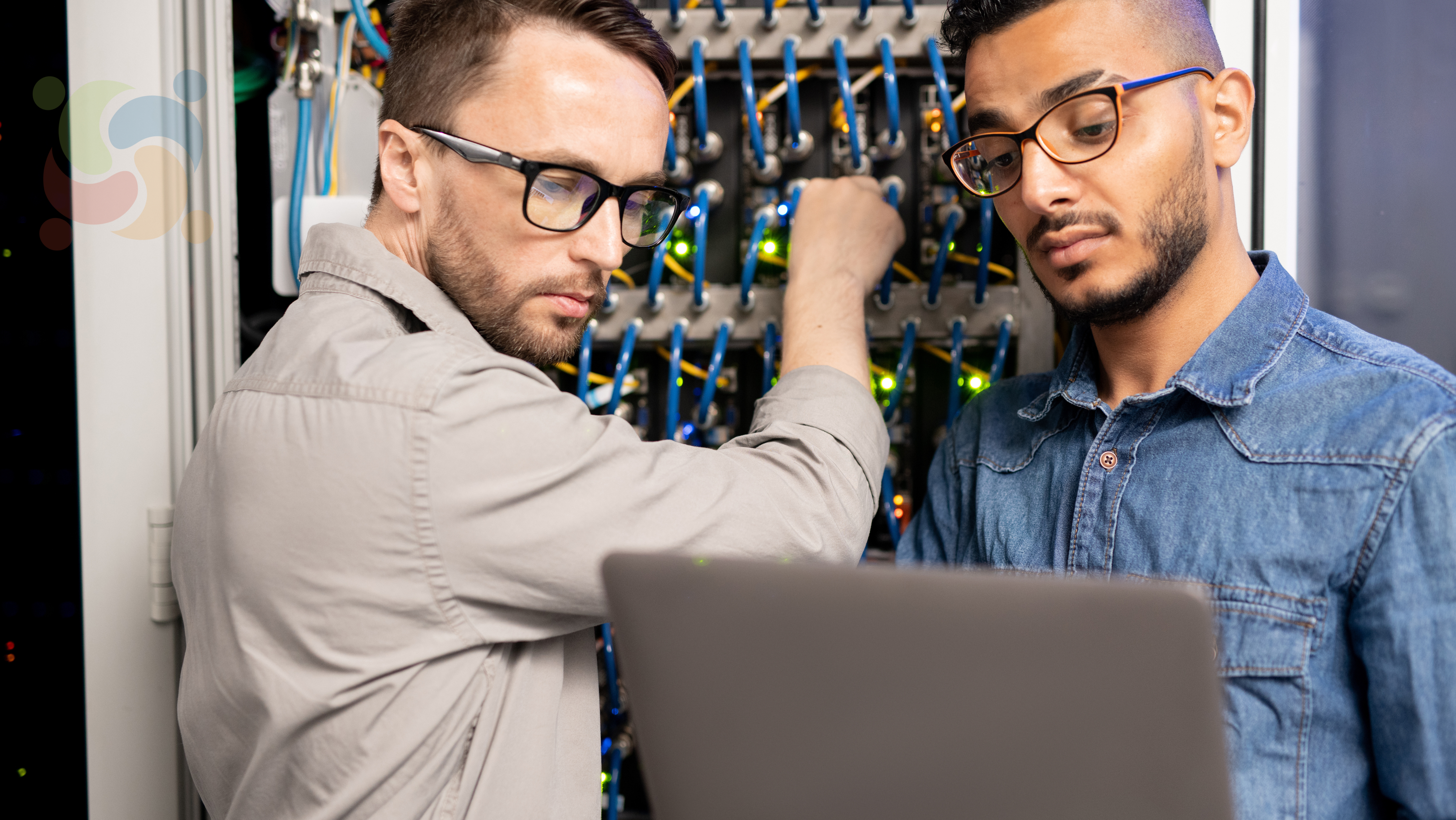 Dois administradores de sistemas trabalhando em um servidor, representando o artigo sobre as '5 razões para usar Linux em servidores ao invés de Windows Server'. A imagem mostra profissionais em um ambiente técnico, com cabos e equipamentos de rede ao fundo.